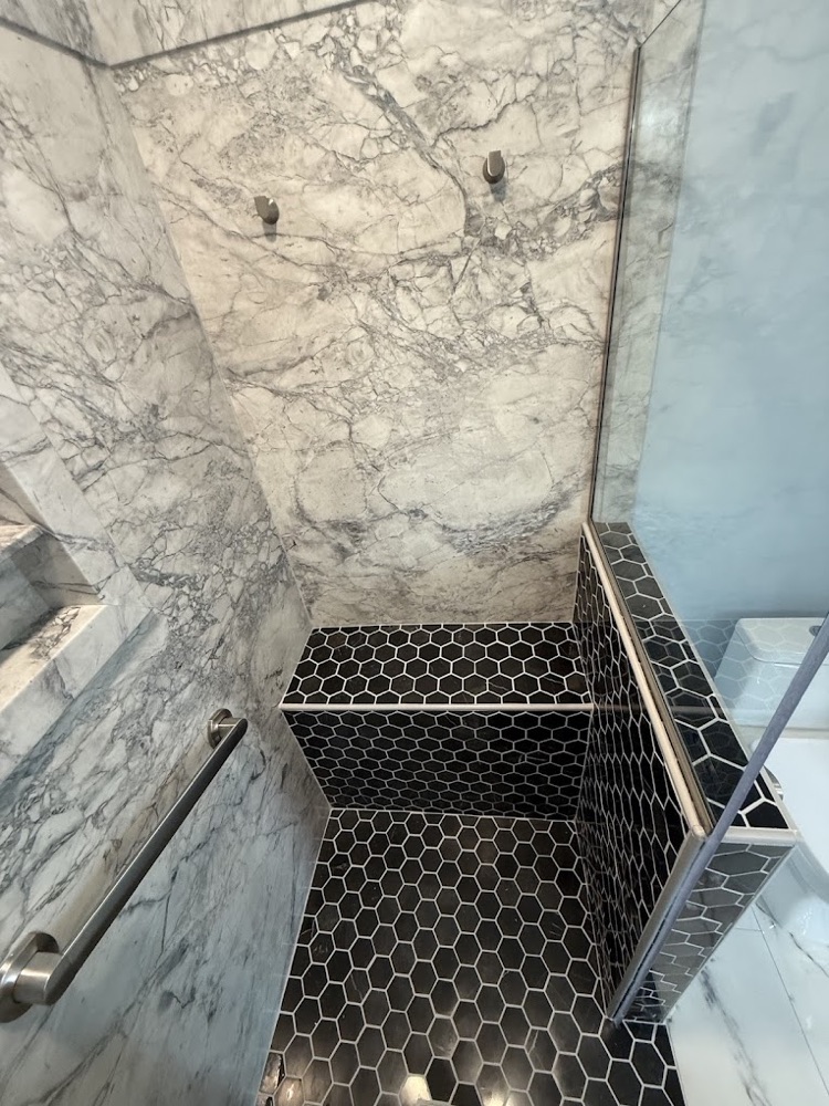 Marble-look walk-in shower with black hex tile bench and floor